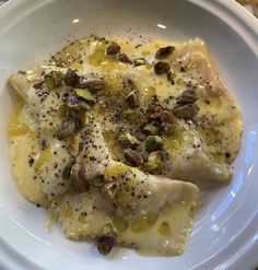 a white plate topped with ravioli covered in cheese and pistachio