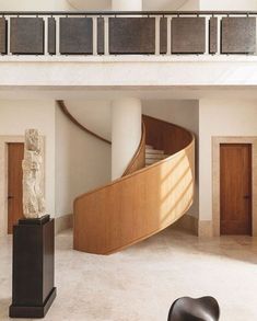 a spiral staircase in the middle of a room with two sculptures on pedestals and a marble busturine next to it