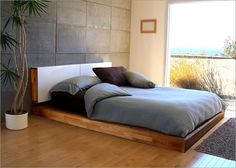 a bed sitting on top of a hard wood floor next to a tall potted plant