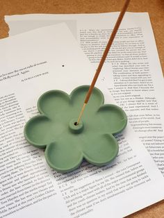 a green flower shaped object sitting on top of an open book with a wooden stick sticking out of it