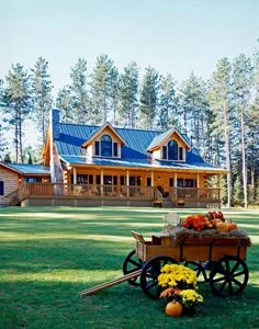 a wagon filled with flowers sitting in front of a large log cabin style house on a lush green field