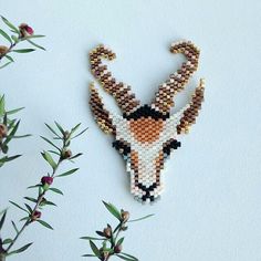 a beaded deer head hanging on a wall next to some leaves and flowers in the foreground