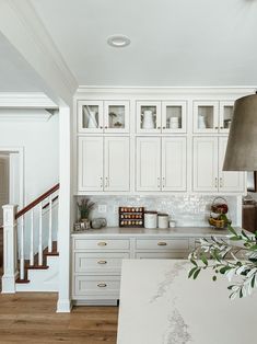 a white kitchen with marble counter tops and wooden stairs leading up to the second floor