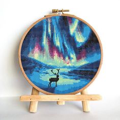 a cross - stitch pattern of a deer in front of an aurora bore