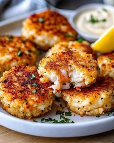 crab cakes on a plate with lemon wedges and mayonnaise next to it