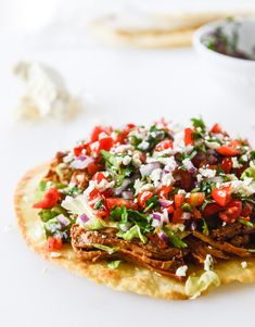 a tortilla topped with meat, lettuce and red onion salsa next to a bowl of sour cream