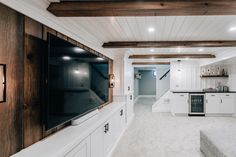 a large kitchen with white cabinets and wood beams on the ceiling, along with an entertainment center