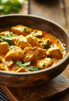 a wooden bowl filled with curry and chicken