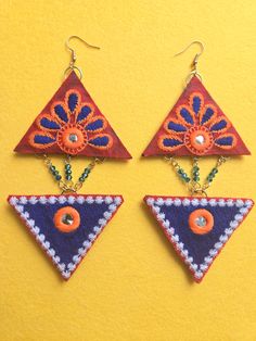 Beaded Blue Petal Embroidered Triangle Earrings Two embroidered fabric stacked triangle shapes arranged in a diamond shape dangle earring. Blue glass beaded chain between triangle shapes. Top triangle has a red background with blue and orange petals surrounding a small circular mirrored center. The bottom triangle is mostly blue with white edges and a small circular mirrored center. Earrings are 5 inches long and 2.5 inches wide with gold 18k gold plated ear wires. Blue Festival Earrings With Latkans, Traditional Handmade Blue Danglers, Blue Handmade Danglers For Festive Occasions, Bohemian Beaded Embroidered Earrings For Festivals, Bohemian Beaded Danglers For Celebration, Bohemian Beaded Danglers For Festive Occasions, Festive Handmade Blue Beaded Earrings, Bohemian Blue Danglers, Bohemian Embroidered Jewelry For Celebration