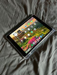 an ipad sitting on top of a bed next to a gray sheet with colorful flowers