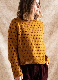 a woman standing in front of a wall wearing a yellow sweater