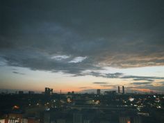 the city skyline is lit up at night with some clouds in the sky above it