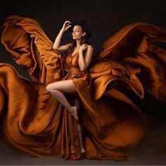 a woman in an orange dress is posing with her hands on her head and arms behind her back