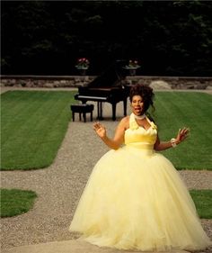 a woman in a yellow and white dress is posing for the camera with her hands out