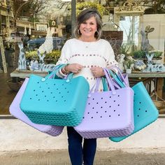 a woman holding two large blue and purple purses in front of a store window