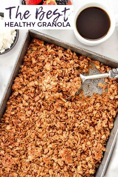 granola in a baking pan with spoons and bowl of fruit on the side