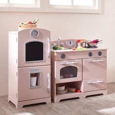 a pink wooden play kitchen set with two ovens and a sink in the corner