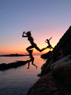 three people jumping off rocks into the water at sunset or dawn with their arms in the air