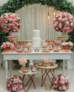 a table topped with lots of pink flowers next to a cake and cupcakes