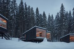 a small cabin in the middle of a snowy forest with lights on it's windows