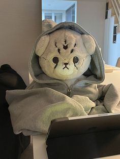 a stuffed animal is sitting in front of a laptop on a table with a blanket over it