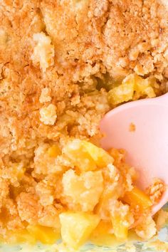 a close up of a casserole dish with a pink spoon in it and crumbs on the side