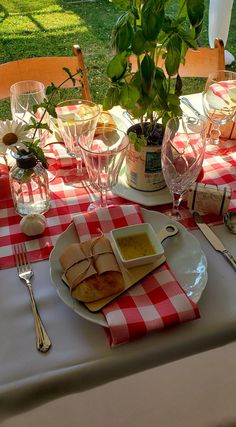 the table is set with plates, silverware, and wine glasses on red and white checkered cloth