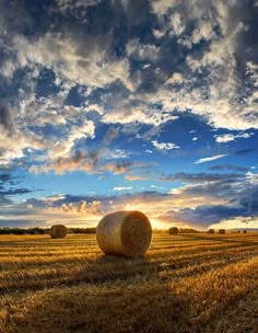 hay bales in the middle of a field at sunset with dramatic clouds above them