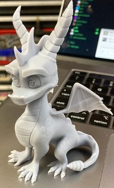 a white dragon figurine sitting on top of a laptop computer desk next to a keyboard