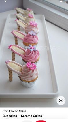 cupcakes with pink frosting and bows are lined up on a white tray