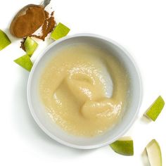 a white bowl filled with liquid next to sliced green apple slices and cinnamon on a white surface