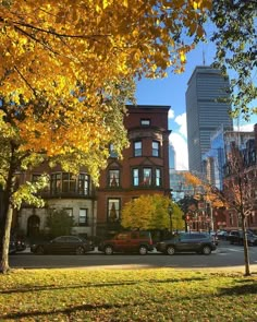 an autumn scene with cars parked on the street and tall buildings in the back ground