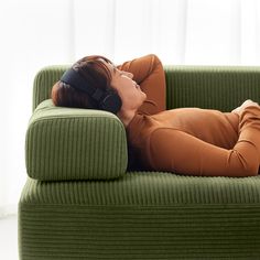 a woman laying on top of a green couch with headphones in her ears and eyes closed