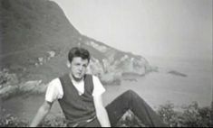 a man sitting on top of a mountain next to the ocean