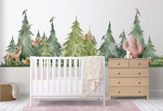 a baby's room with a crib, dresser and wall mural depicting trees