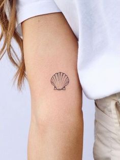 a woman's arm with a small shell tattoo on the left side of her right arm