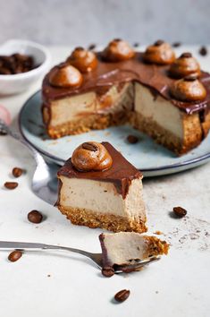 a piece of cheesecake on a plate with a fork next to it and a bowl of nuts in the background