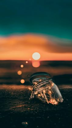 a jar filled with lights sitting on top of a sandy beach