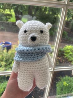 a hand holding a small white crocheted teddy bear with a blue scarf around it's neck