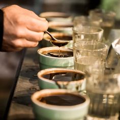 a person is spooning coffee into cups lined up on a table with other glasses