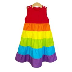 Tiered rainbow dress. Made with 100% premium quality cotton. Fully lined bodice and skirt. Rainbow dress made from a red bodice and tired skirt of rainbow colours. The tiered skirt creates a beautiful shape - perfect for twirling! KAM Snap fasting on the shoulders for quick and easy dressing. This dress sits below the knee, almost ankle length. Please check our size guide based on child's height to make sure you are ordering the best fit for your child.  0-3 months: up to 62cm  3-6 months: 62cm - 68cm 6-9 months: 68cm - 74cm 9-12 months: 74cm - 80cm 12-18 months: 80cm - 86cm 18-24 months: 86cm - 92cm 2-3 years: 92cm - 98cm 3-4 years: 98cm - 104cm 4-5 years: 104cm - 110cm 5-6cm: 110m - 116cm 6-7cm: 116cm - 122cm 7-8cm: 122-128cm Playful Multicolor Tiered Dress, Playful Rainbow Dress With Ruffles, Rainbow Cotton Dress For Playtime, Playful Rainbow Cotton Dresses, Rainbow Cotton Playtime Dress, Rainbow Cotton Dresses For Spring, Spring Rainbow Cotton Dresses, Rainbow Summer Dress For Playtime, Rainbow Summer Dresses For Playtime