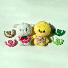 three small stuffed animals sitting next to each other on a white surface with green and pink crocheted flowers