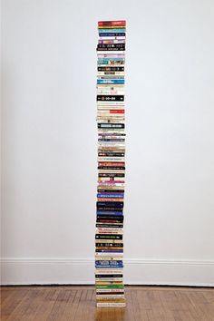 a tall stack of books sitting on top of a wooden floor next to a white wall