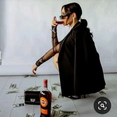 a woman sitting on the floor with money around her and a bottle of booze in front of her