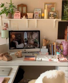 a desk with a computer, phone and other office supplies on top of it in front of a white wall