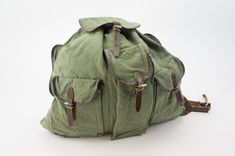 an old green canvas backpack with leather straps and buckles on the front, sitting against a white background