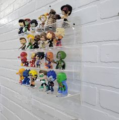 a bunch of action figures are hanging on a white brick wall in a display case