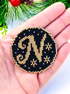 a hand holding a black and gold beaded monogrammed brooch on it's palm