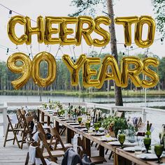 a long table with chairs and balloons that say cheers to 90 years in gold letters