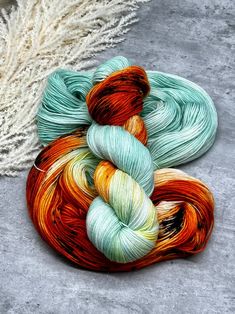 two skeins of yarn sitting on the ground next to some white and orange flowers